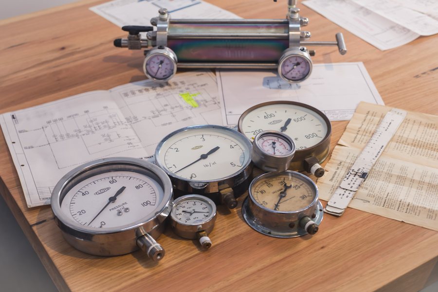 Pressure gauges and a sample cylinder on the workshop bench with engineering drawings